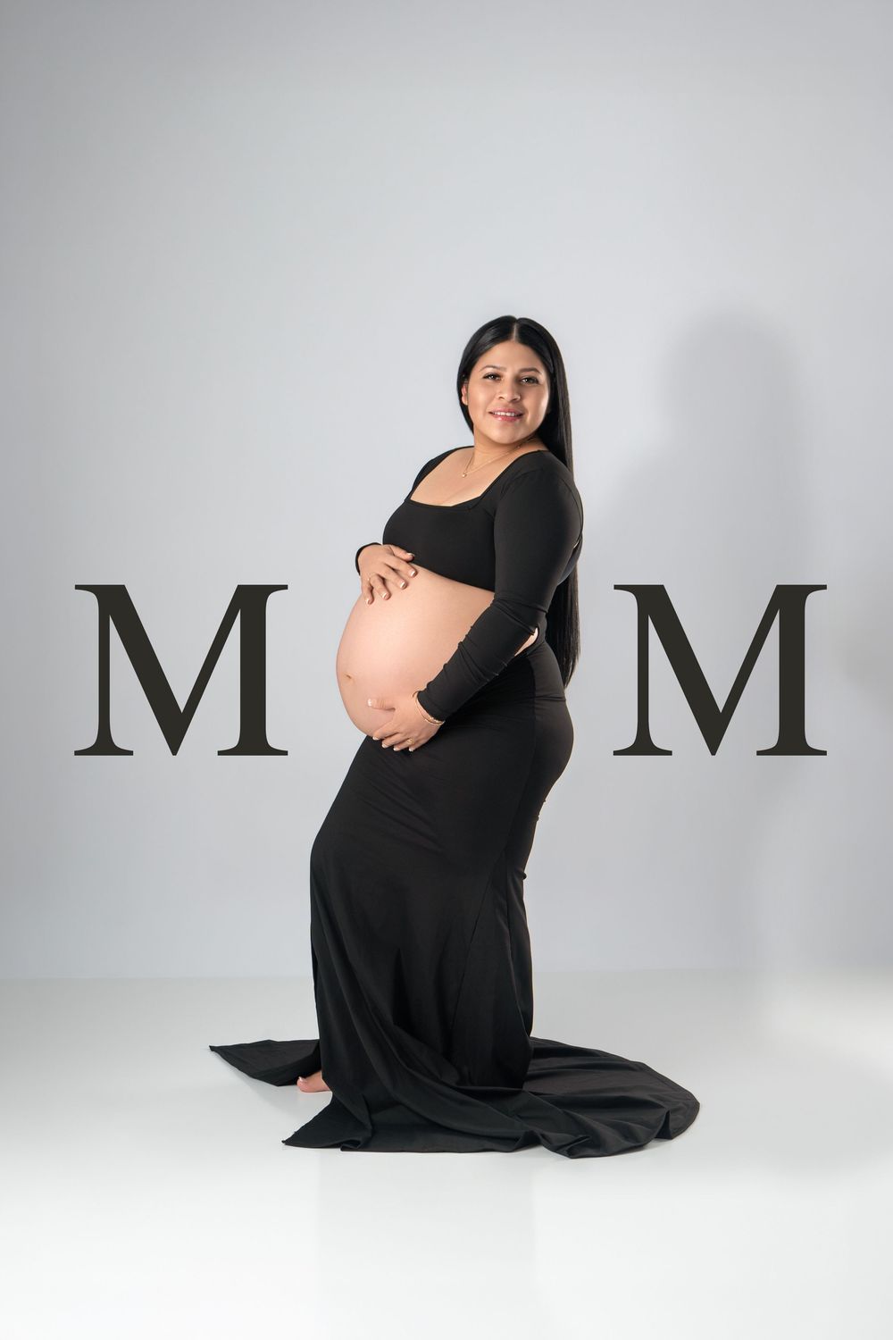 Pregnant woman in black maternity gown posing with MOM text overlay on light gray background.