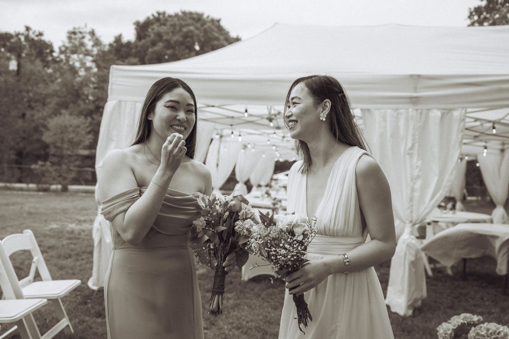 Two women laugh together in black and white photo at outdoor wedding with tent backdrop.