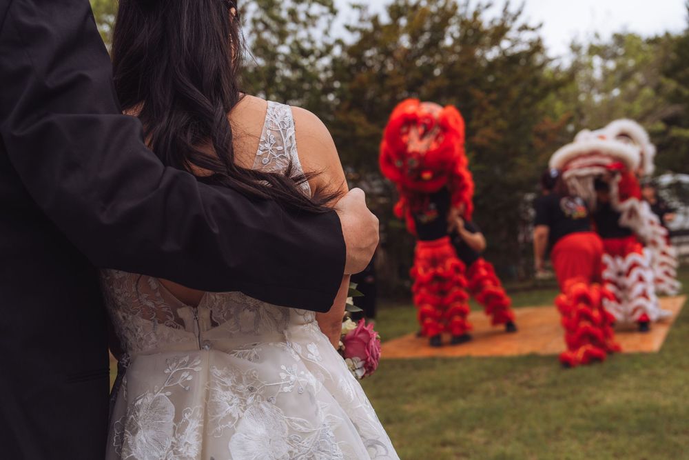 Bride and groom watch a traditional red Chinese lion dance performance at an outdoor wedding ceremony.