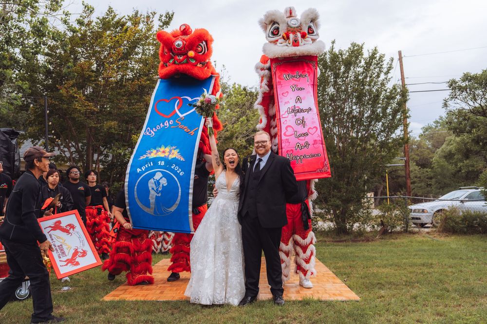 Bride and groom pose with colorful Chinese lion dancers at outdoor wedding celebration.