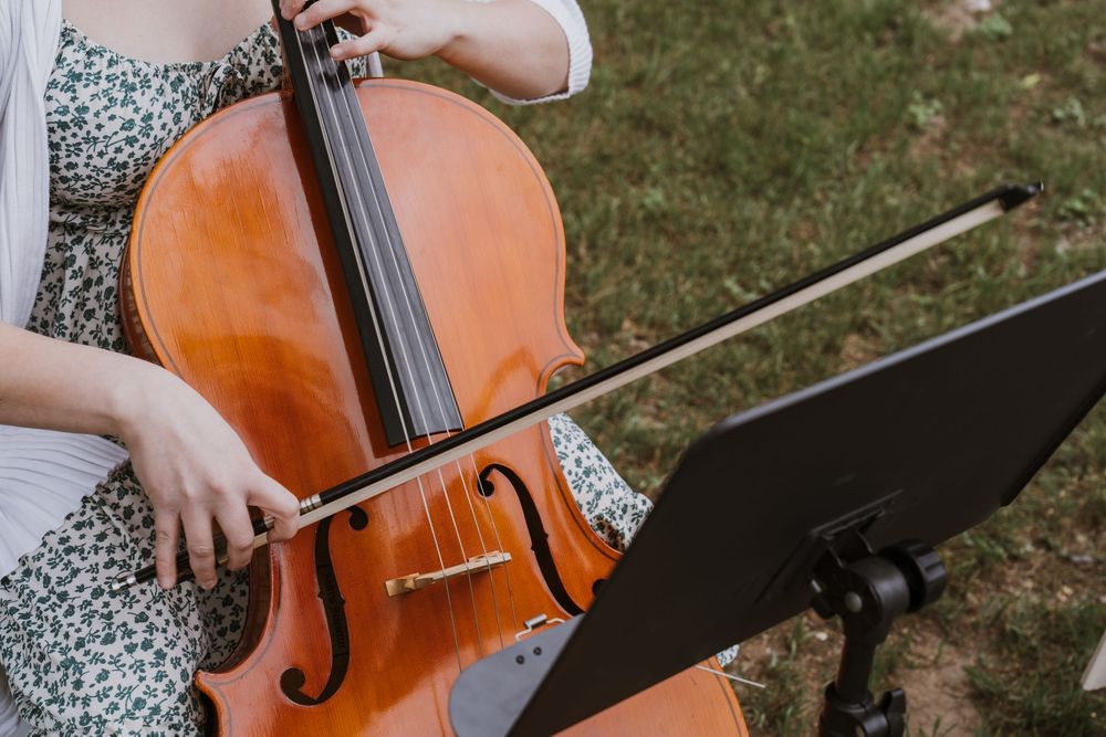 A cellist plays cello outdoors, reading sheet music on a stand during an elegant garden performance.