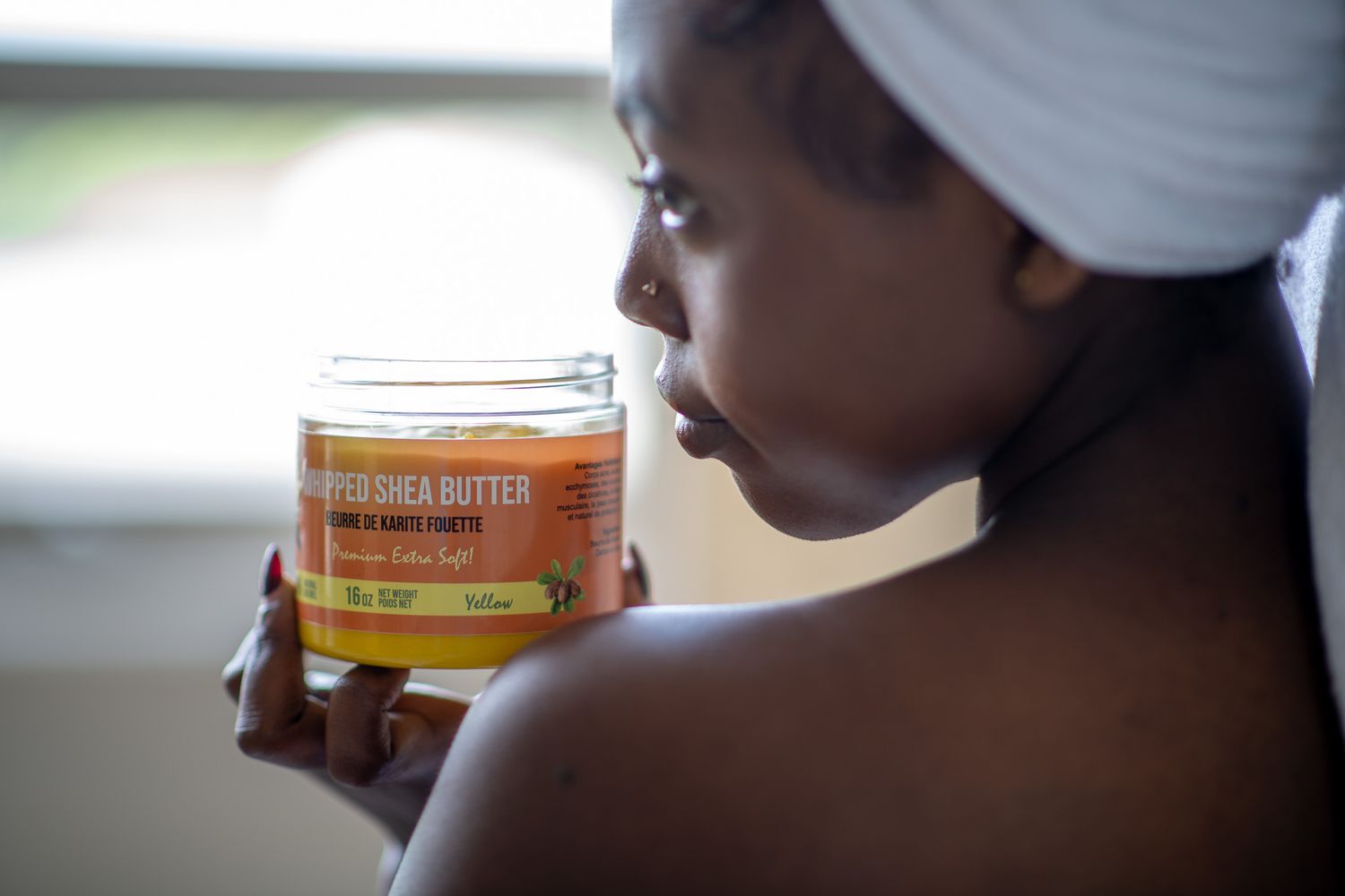 Woman with white head wrap smelling a jar of pure shea butter skincare product.