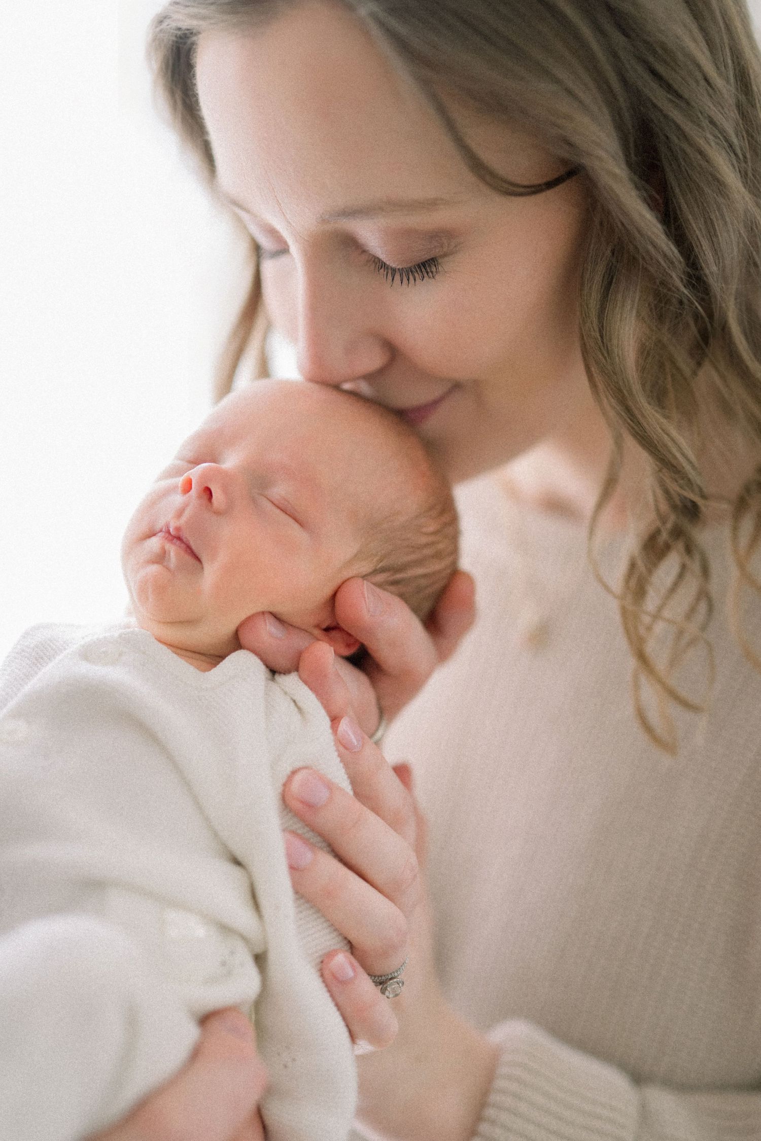 A mother tenderly kisses her sleeping newborn baby wrapped in white taken at an in-home newborn session