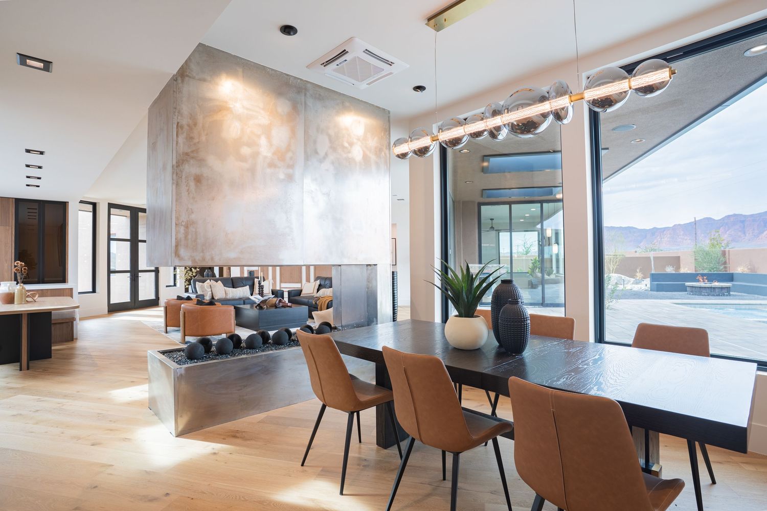 Modern dining room with leather chairs, black table, linear pendant light, stone fireplace, and mountain views.