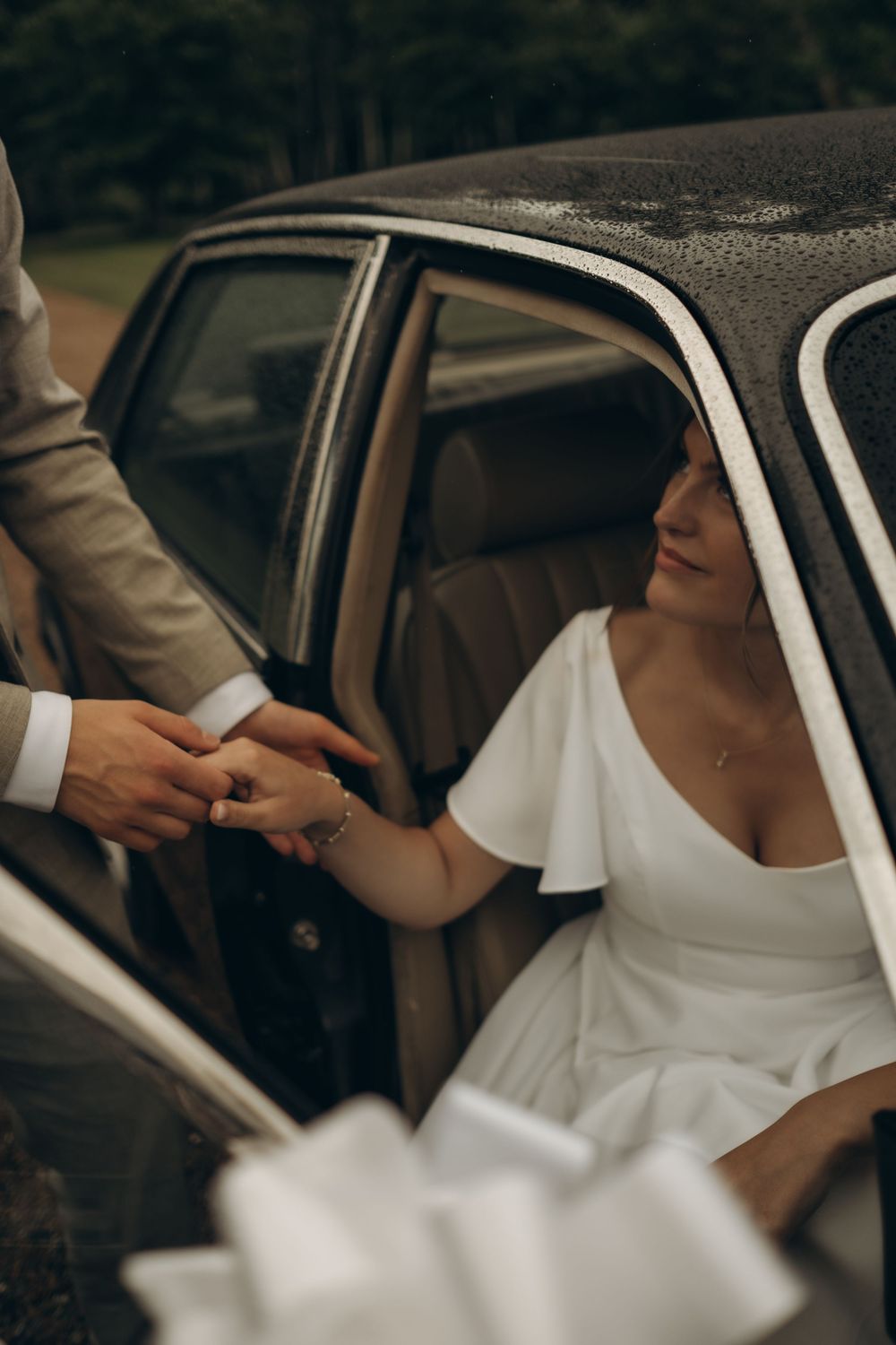groom helping bride out of vintage car during storytelling wedding portrait shoot in Stockholm