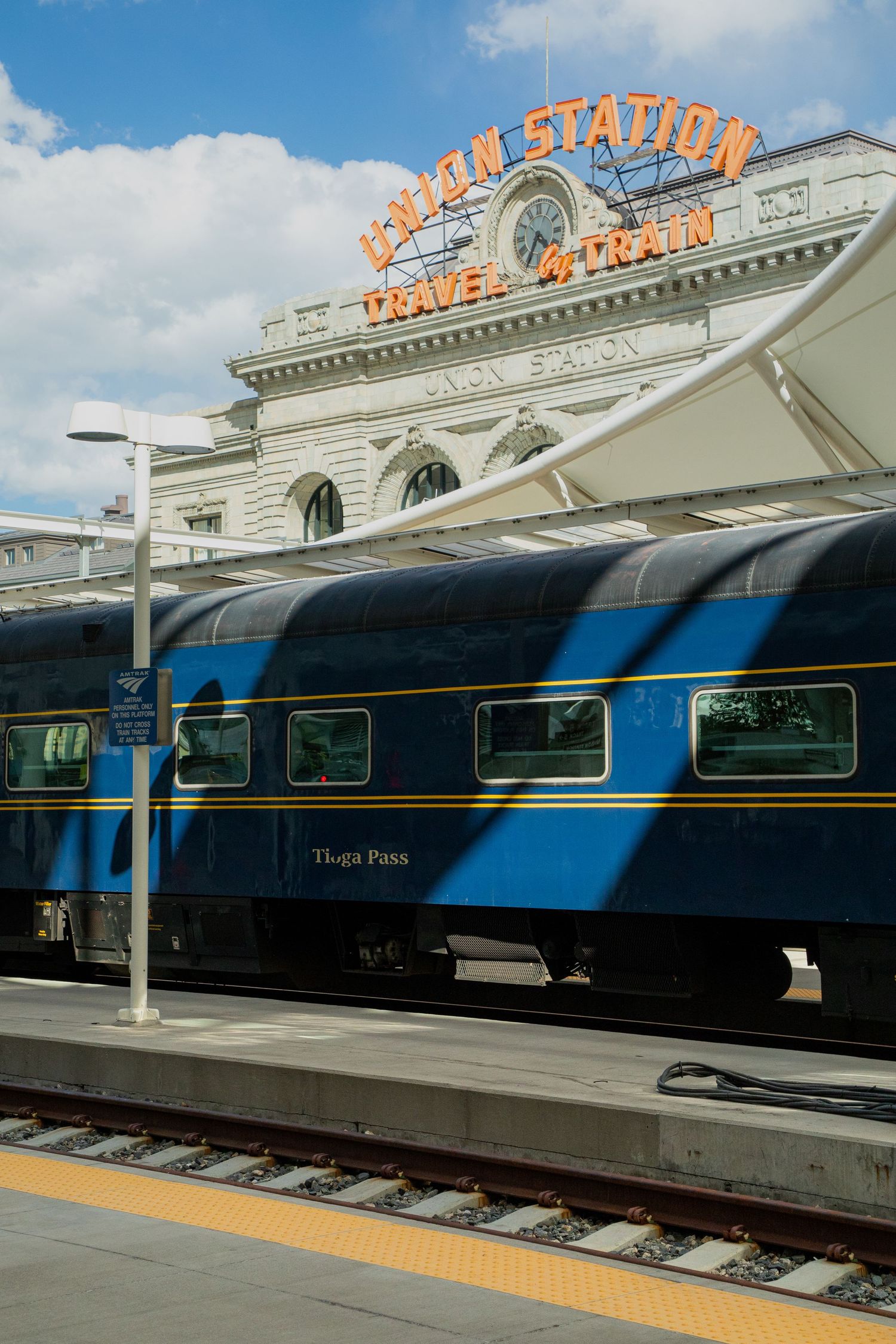 Blue train car parked at Denver Union Station platform with iconic neon sign and historic white facade visible.
