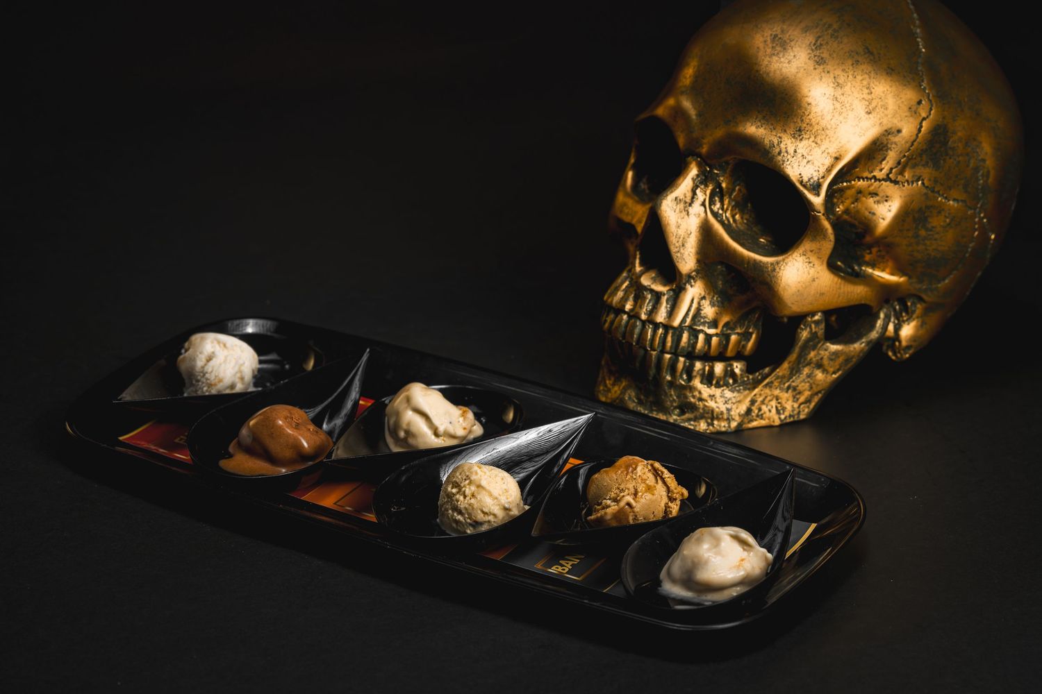 Golden skull beside a black tray of assorted chocolate truffles on a dark background.
