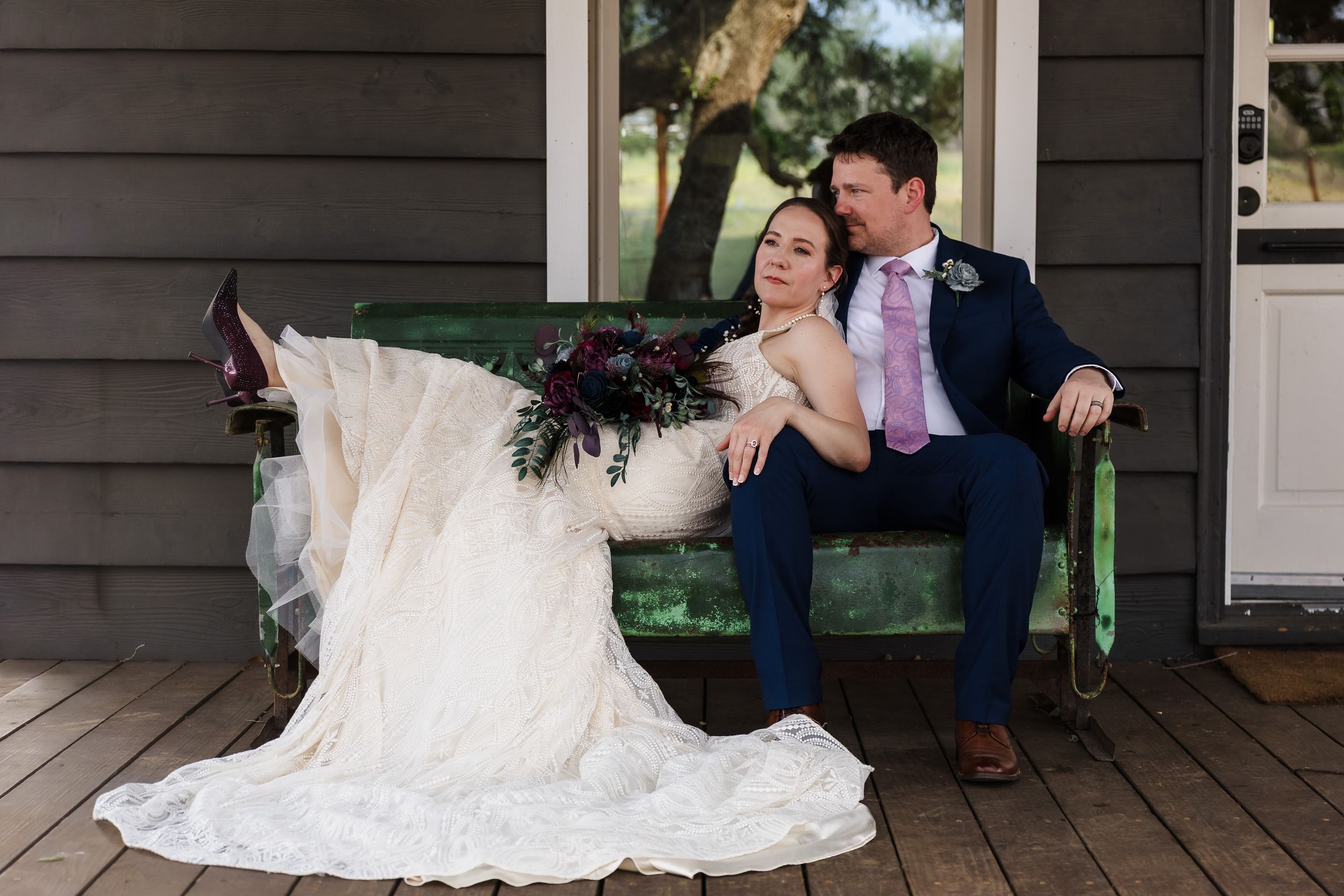 Editorial lifestyle wedding portrait of a bride and groom posing on a vintage green bench on a porch in Buda, Texas.