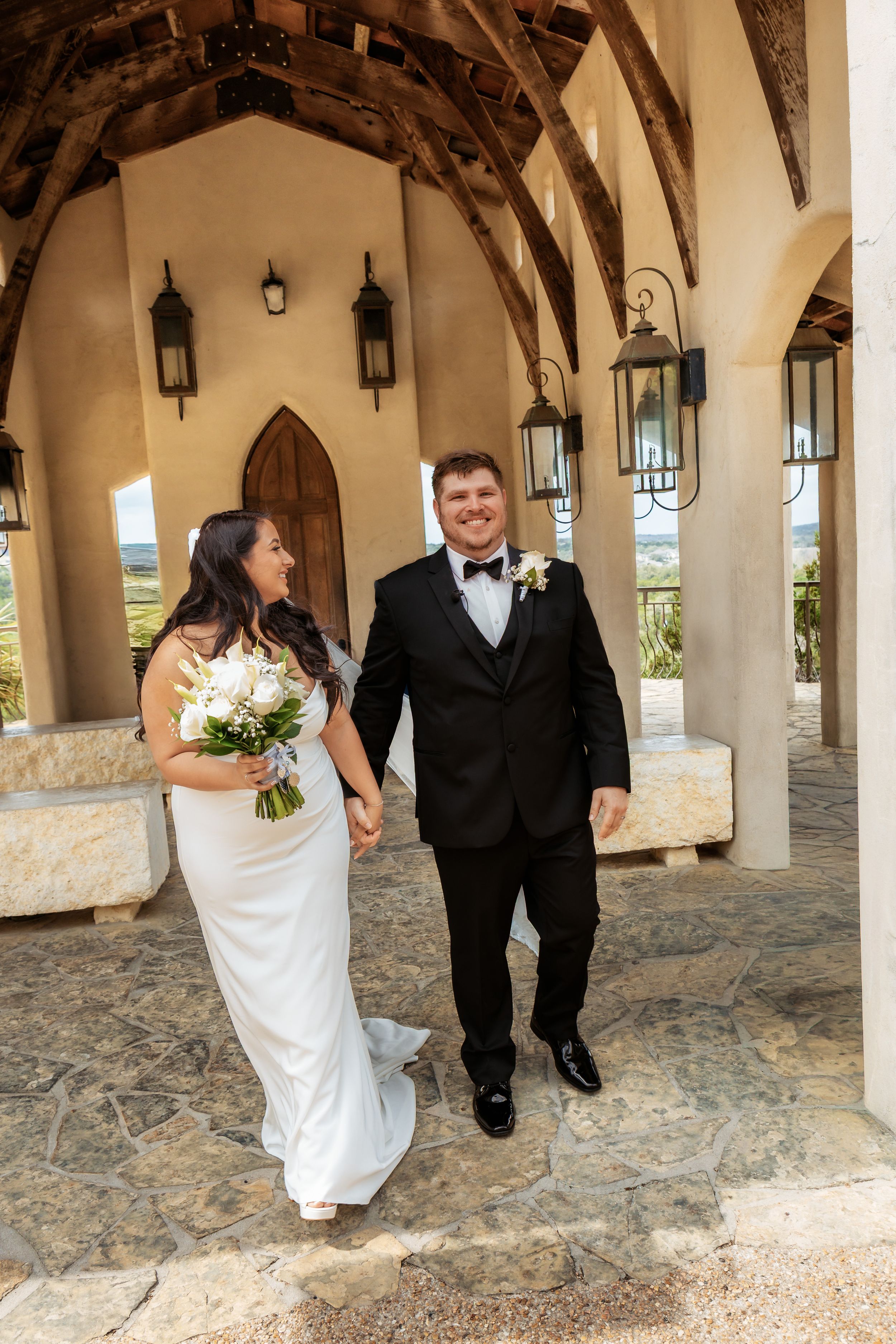 A wedding couple walking through an elegant stone archway at an Austin wedding venue, showcasing natural light and refined architecture.
