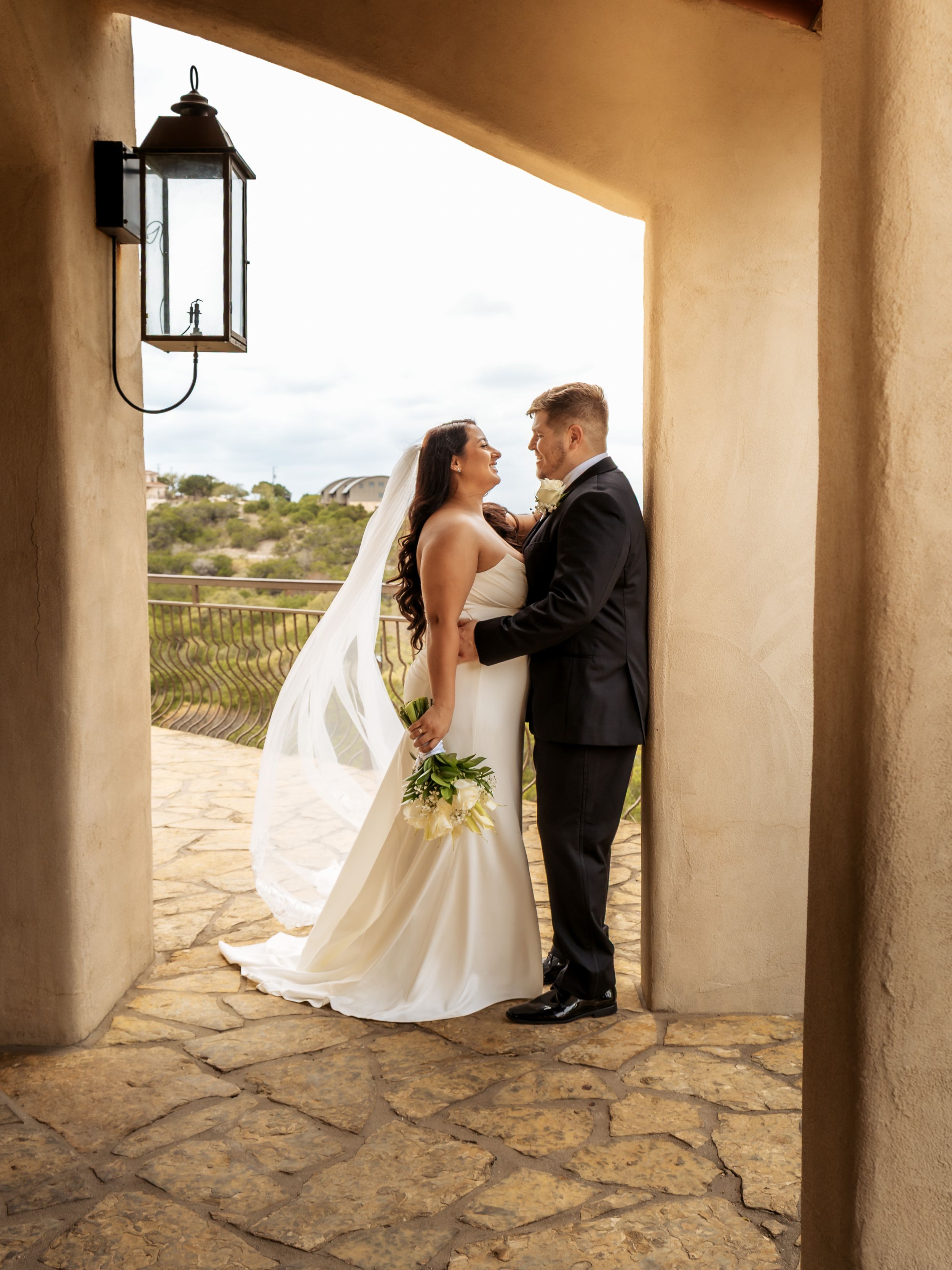 Intimate portrait of a bride and groom embracing in a sunlit stone archway overlooking the Texas Hill Country.