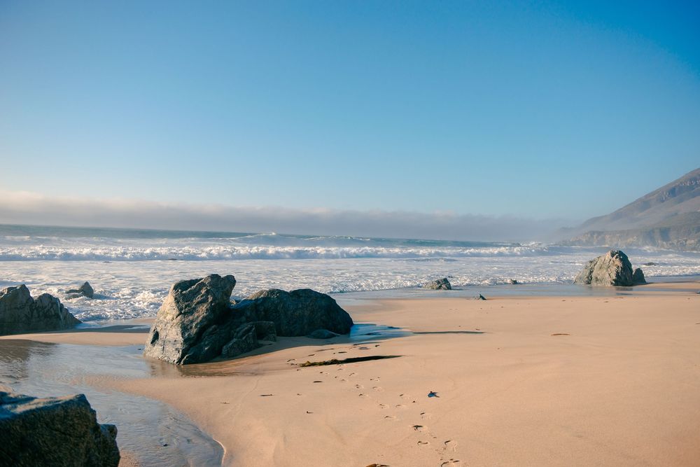 Rocky beach with golden sand, ocean waves, and a clear blue sky on a serene coastal landscape.