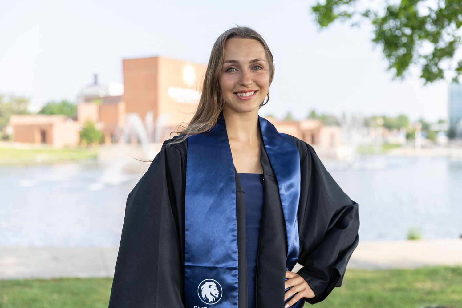 woman wearing graduation gown and stole standing in front of the university