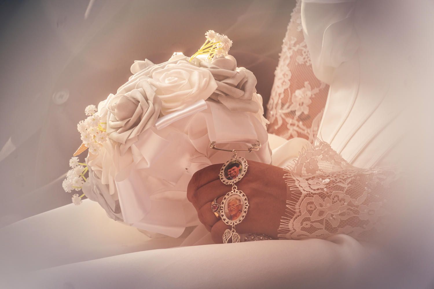Elegant bridal bouquet of white roses with lace details and vintage jewelry accessories in soft romantic lighting.