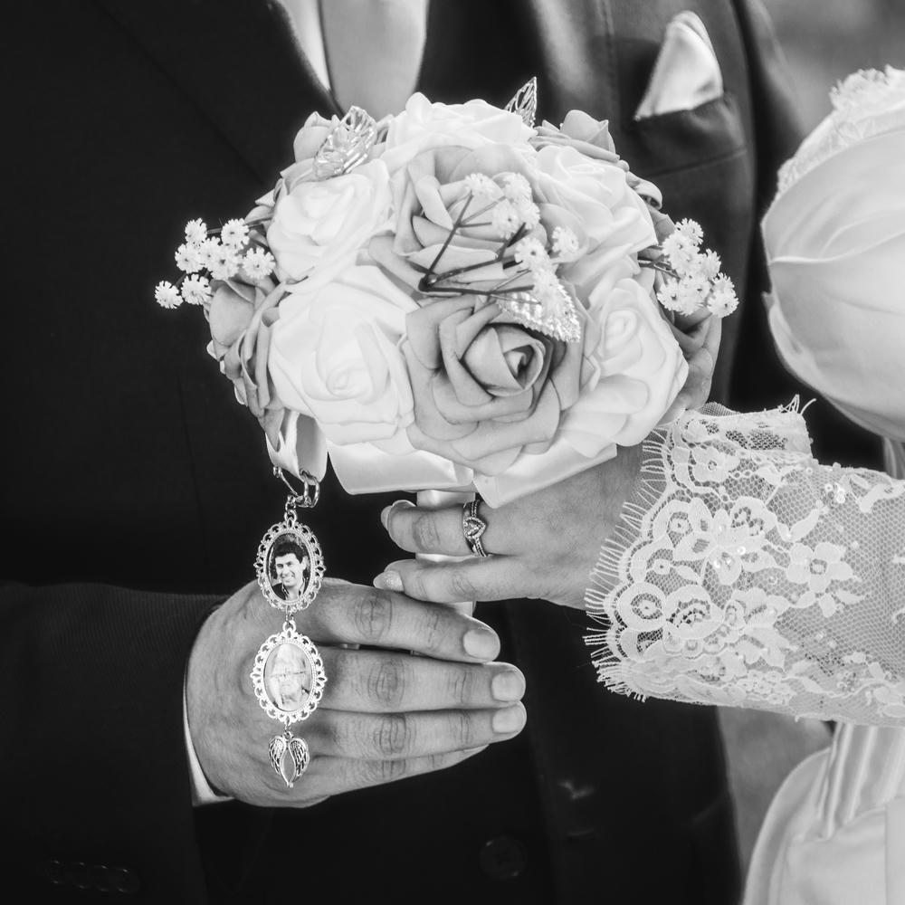 Black and white wedding photo of bride and groom holding white rose bouquet with vintage locket charm.