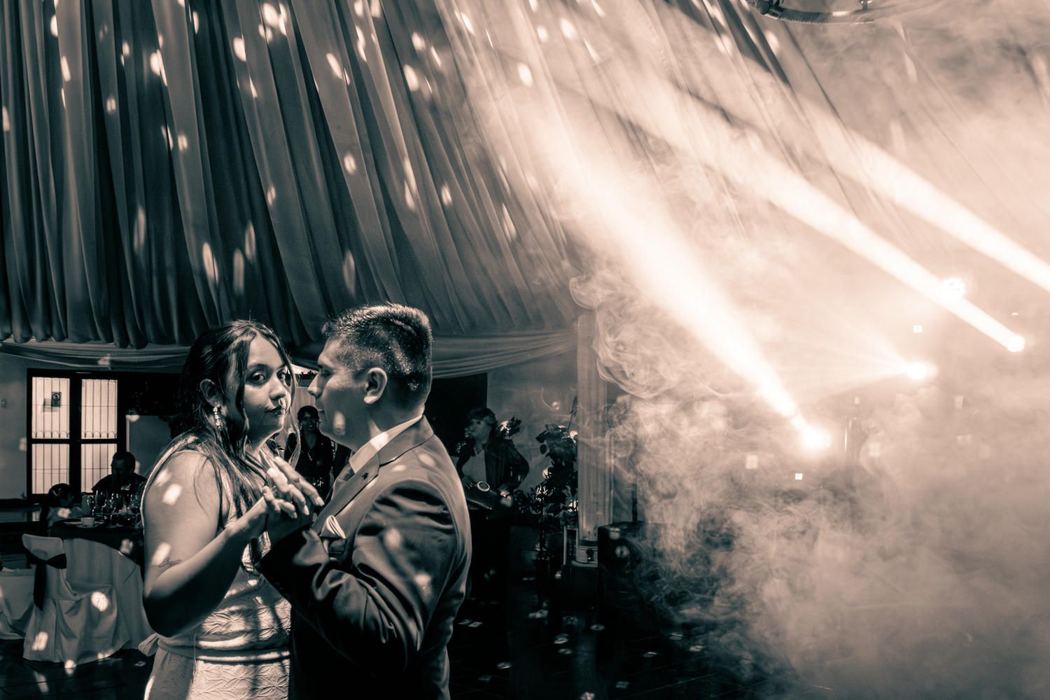 Couple shares romantic first dance surrounded by dramatic fog and spotlights at wedding.