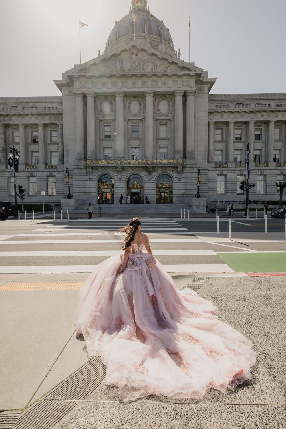 Woman in pink ballgown wedding dress poses in front of San Francisco City Hall on a sunny day.