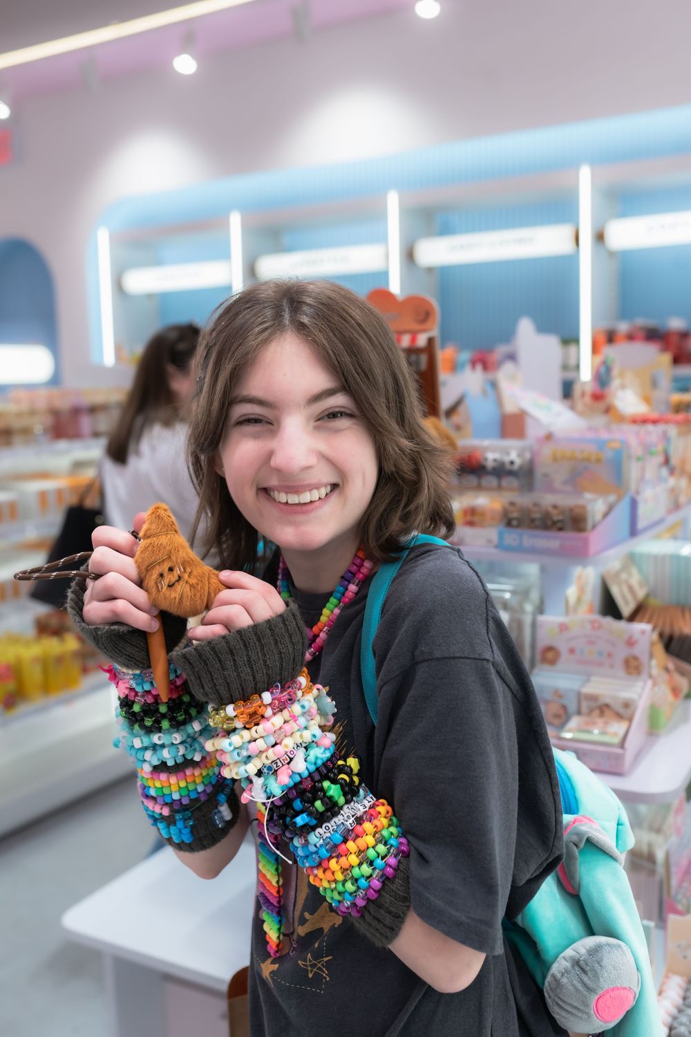 Smiling teen girl wearing colorful beaded bracelets holds a plush toy in a bright gift shop.