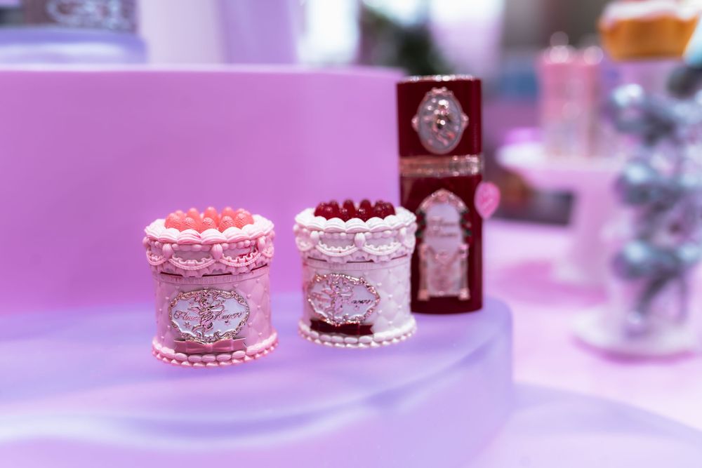 Two elegant pink decorative cake boxes with silver detailing displayed on a pastel purple tiered stand.