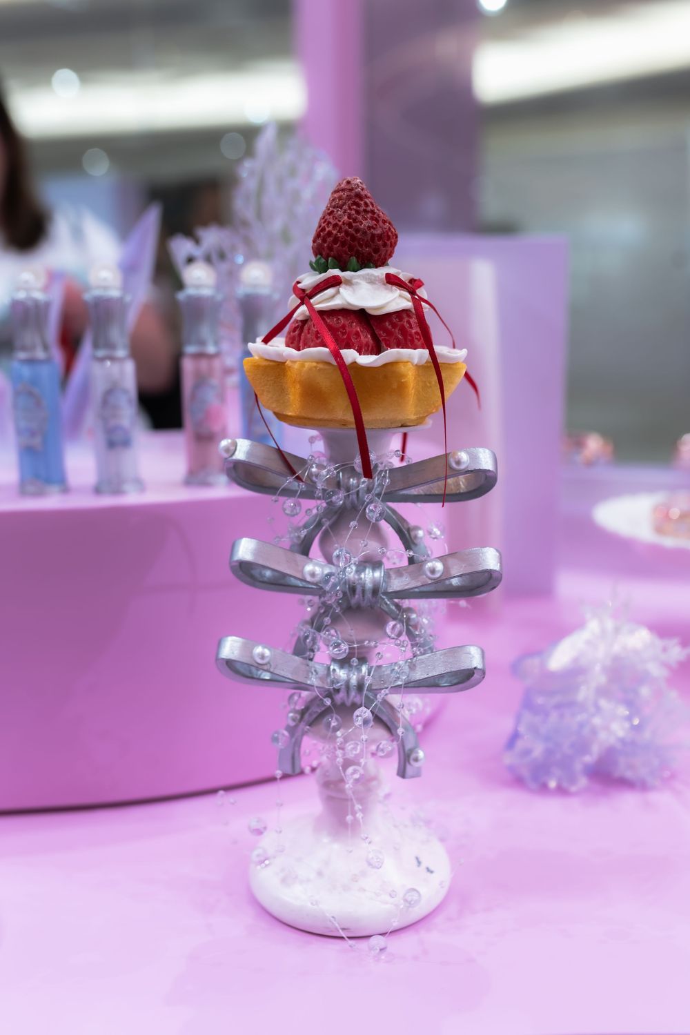 Elegant dessert tart topped with raspberries displayed on ornate silver bow stand on pink table.