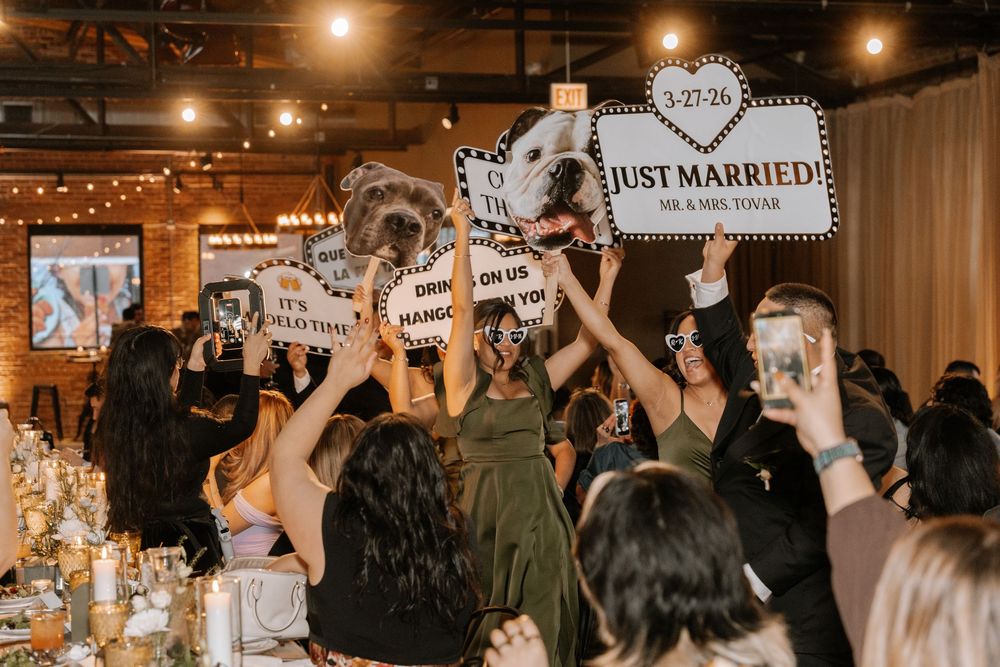 Wedding guests raise fun photo booth signs including Just Married at a romantic candlelit reception venue.