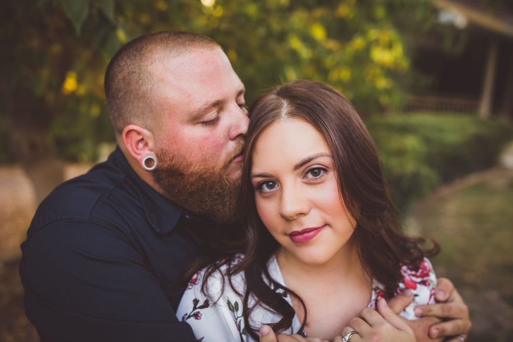 A couple shares a tender moment outdoors, man kissing womans cheek in a romantic portrait.