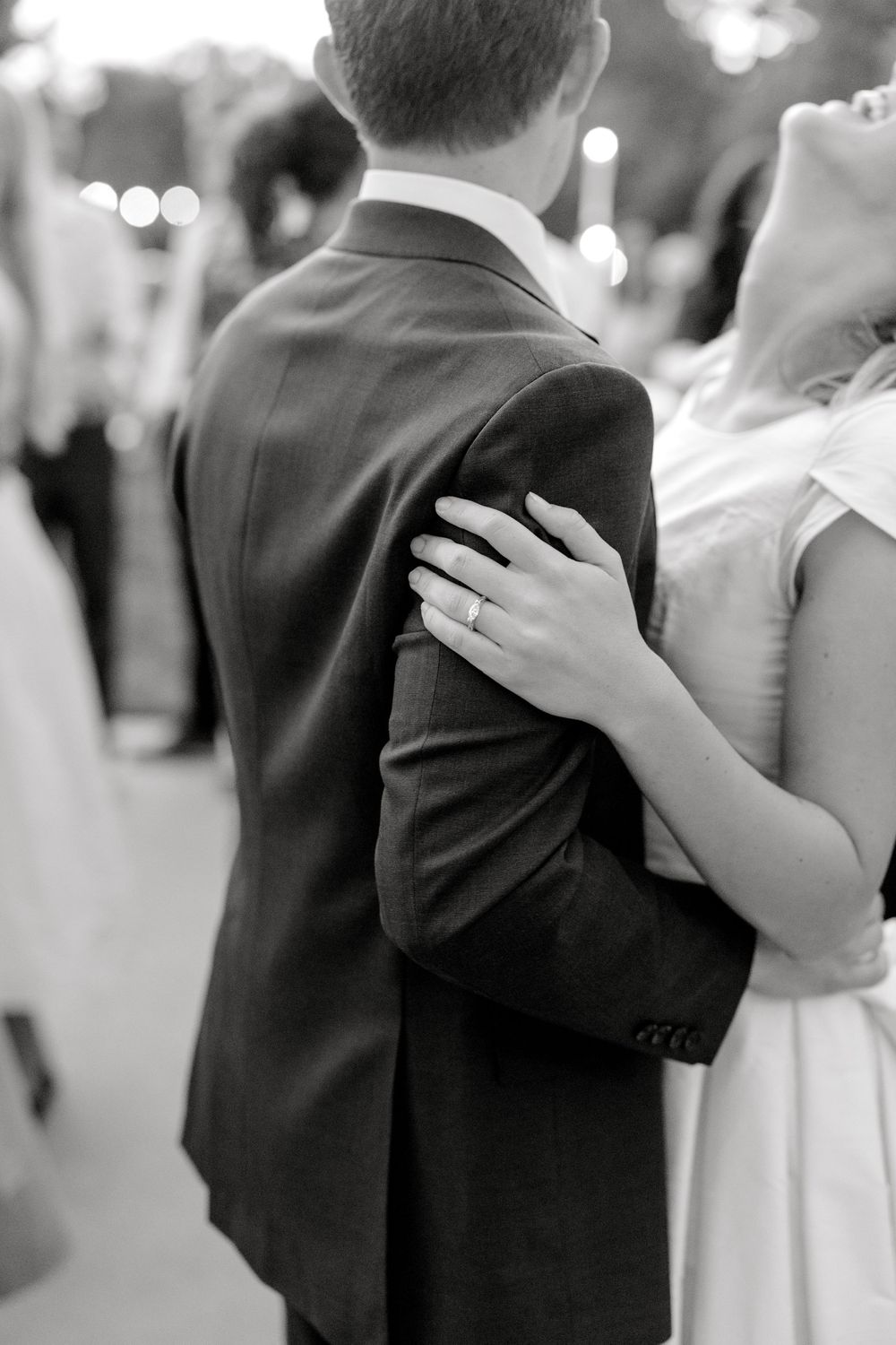 Black and white photo of bride placing hand with wedding ring on grooms suit jacket.