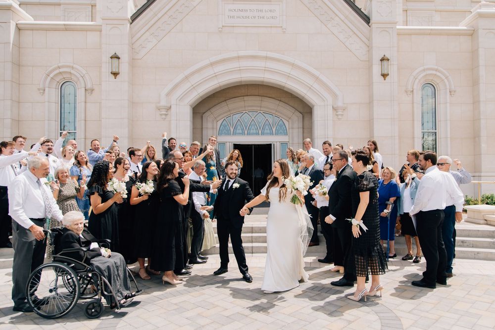 Wedding party celebrating outside a church with guests cheering on sunny day.