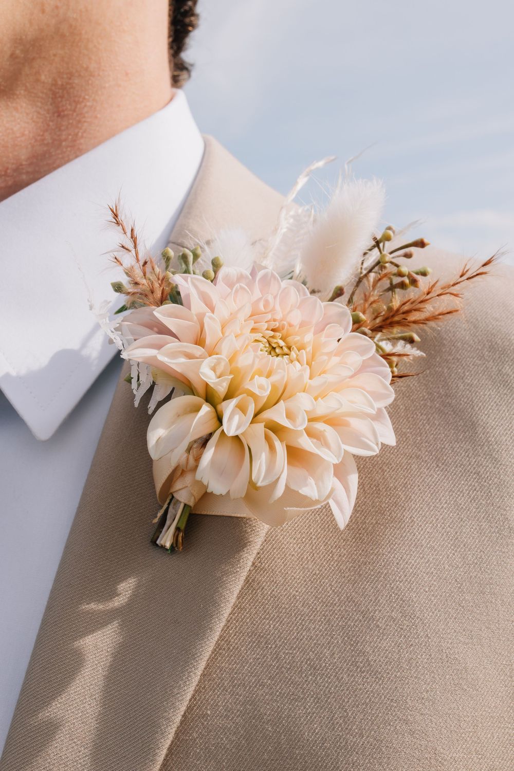Close-up of elegant peach dahlia boutonniere on groom's beige suit lapel at wedding.