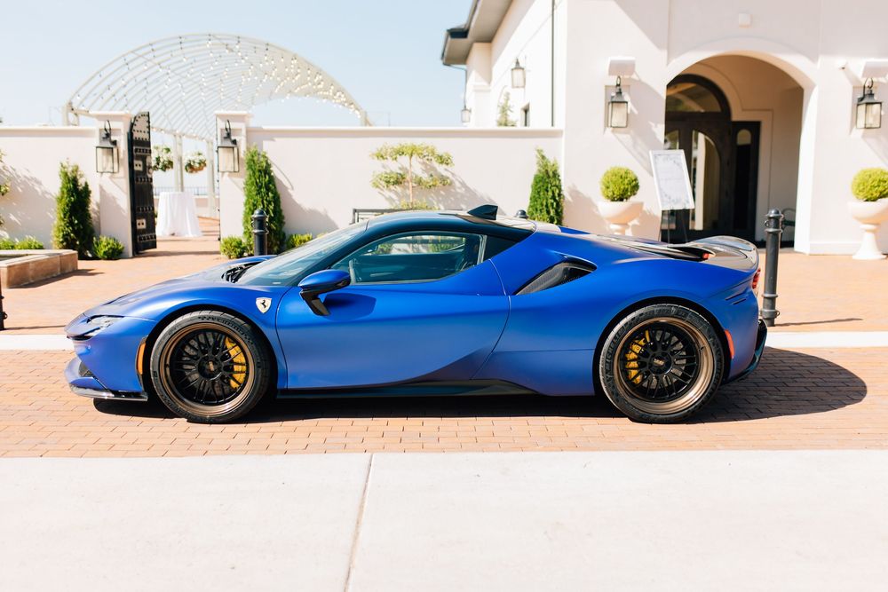 Stunning blue Ferrari sports car parked outside luxury white estate on sunny day.