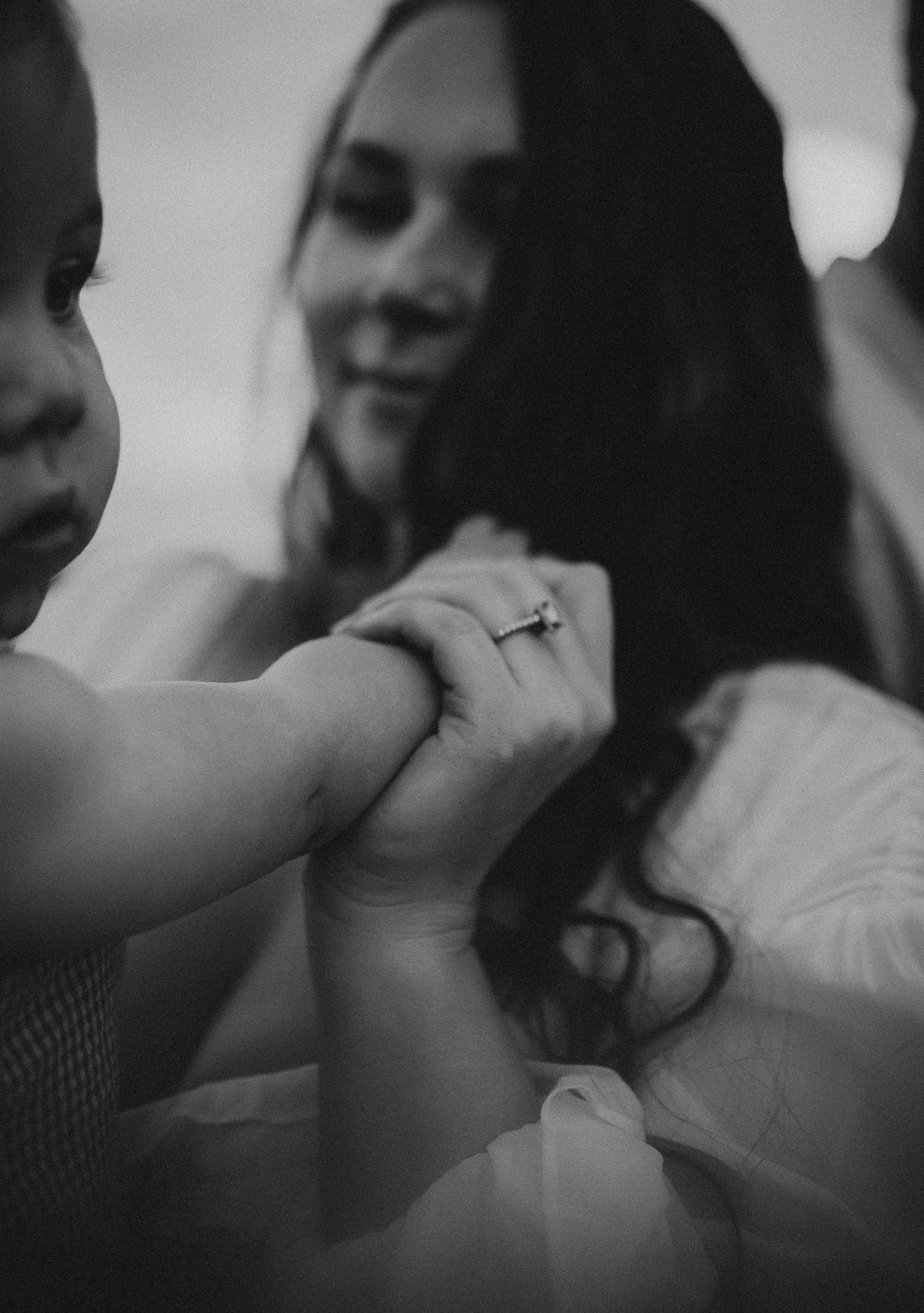 Black and white photo of a smiling woman holding a small child's hand, wearing a diamond wedding ring.