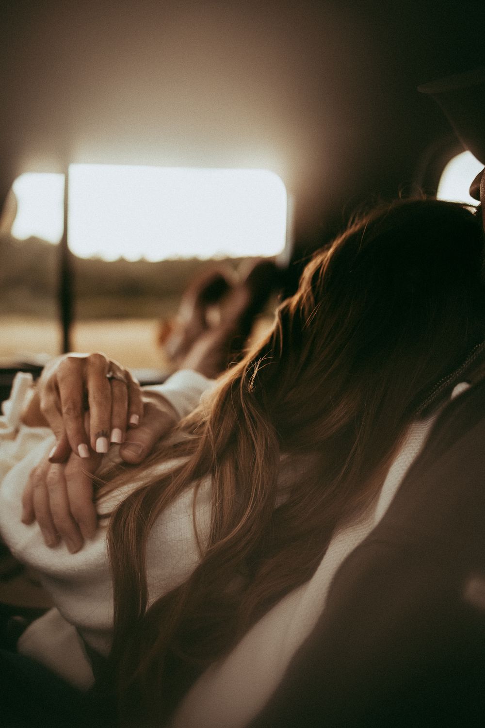 A woman with long blonde hair holds hands with husband in the backseat of a car at golden hour.