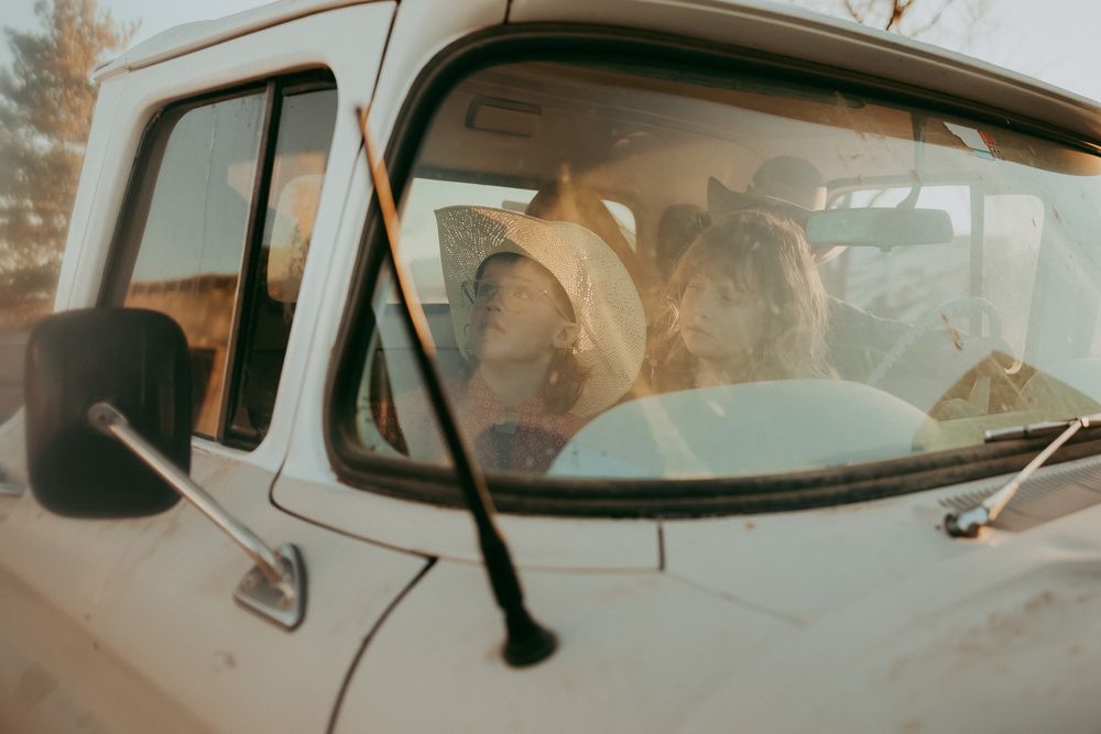 Family sits together inside a vintage white pickup truck, bathed in warm golden sunlight.