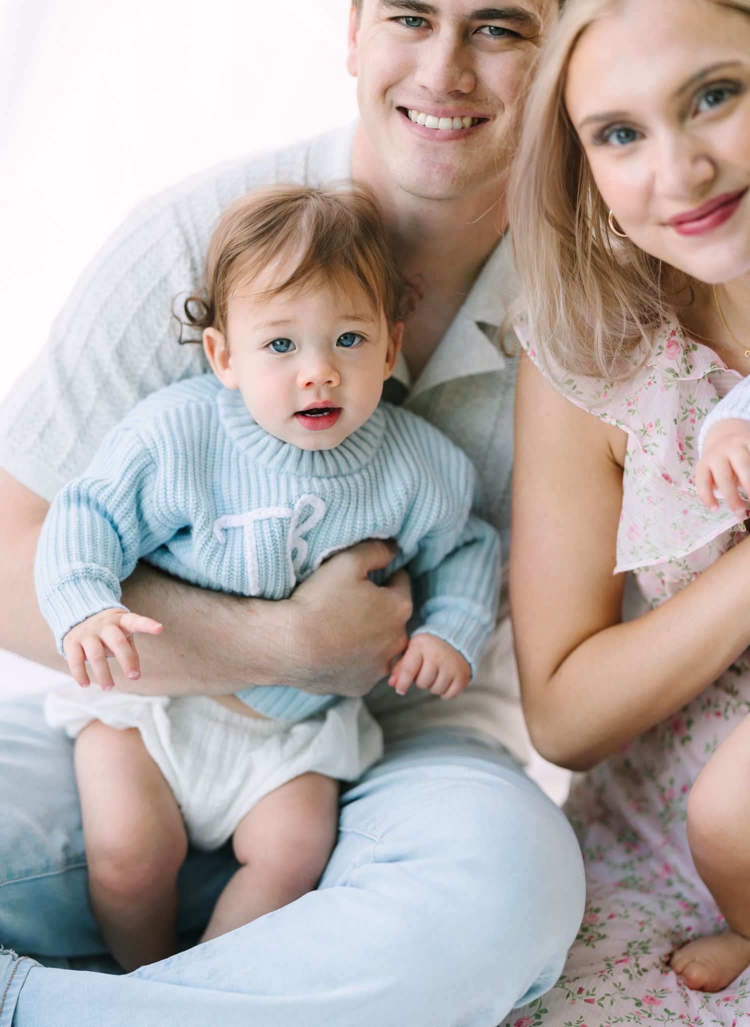 Happy young family with smiling parents holding an adorable baby in a blue knit sweater during a portrait session.