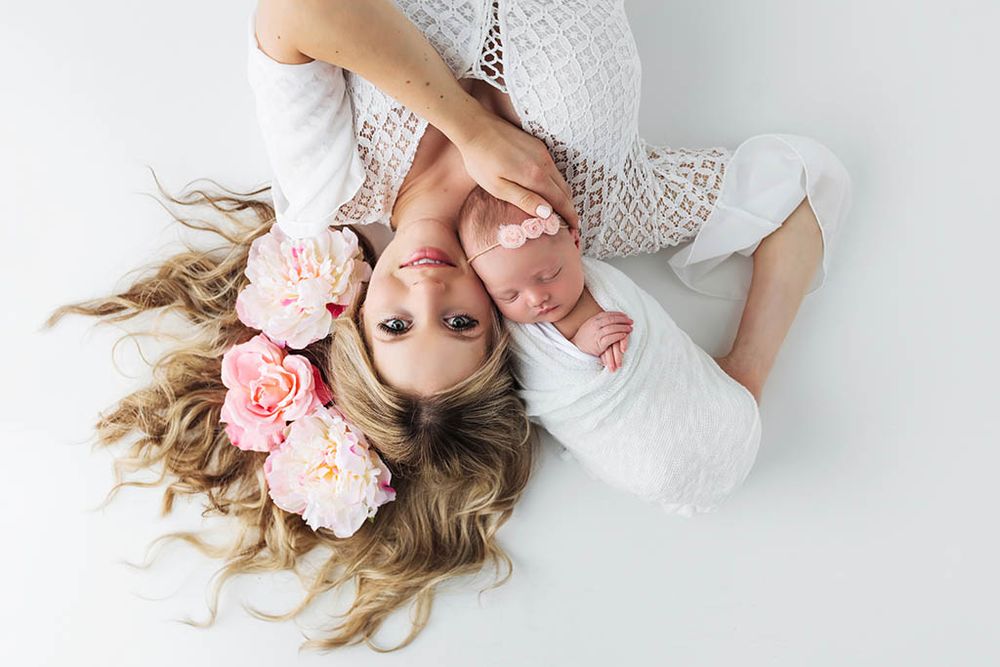 Beautiful mom and baby photo by Winchester baby photographer - Mom with flowers in her hair lying down holding newborn daughter.