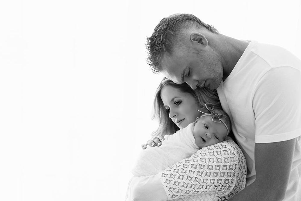 Black and white photo of parents snuggling their newborn baby girl, a touching family portrait by professional Winchester baby photographer.