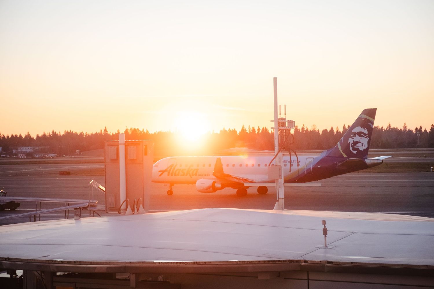 Alaska Airlines plane on tarmac at sunset with golden hour light glowing behind aircraft at airport.