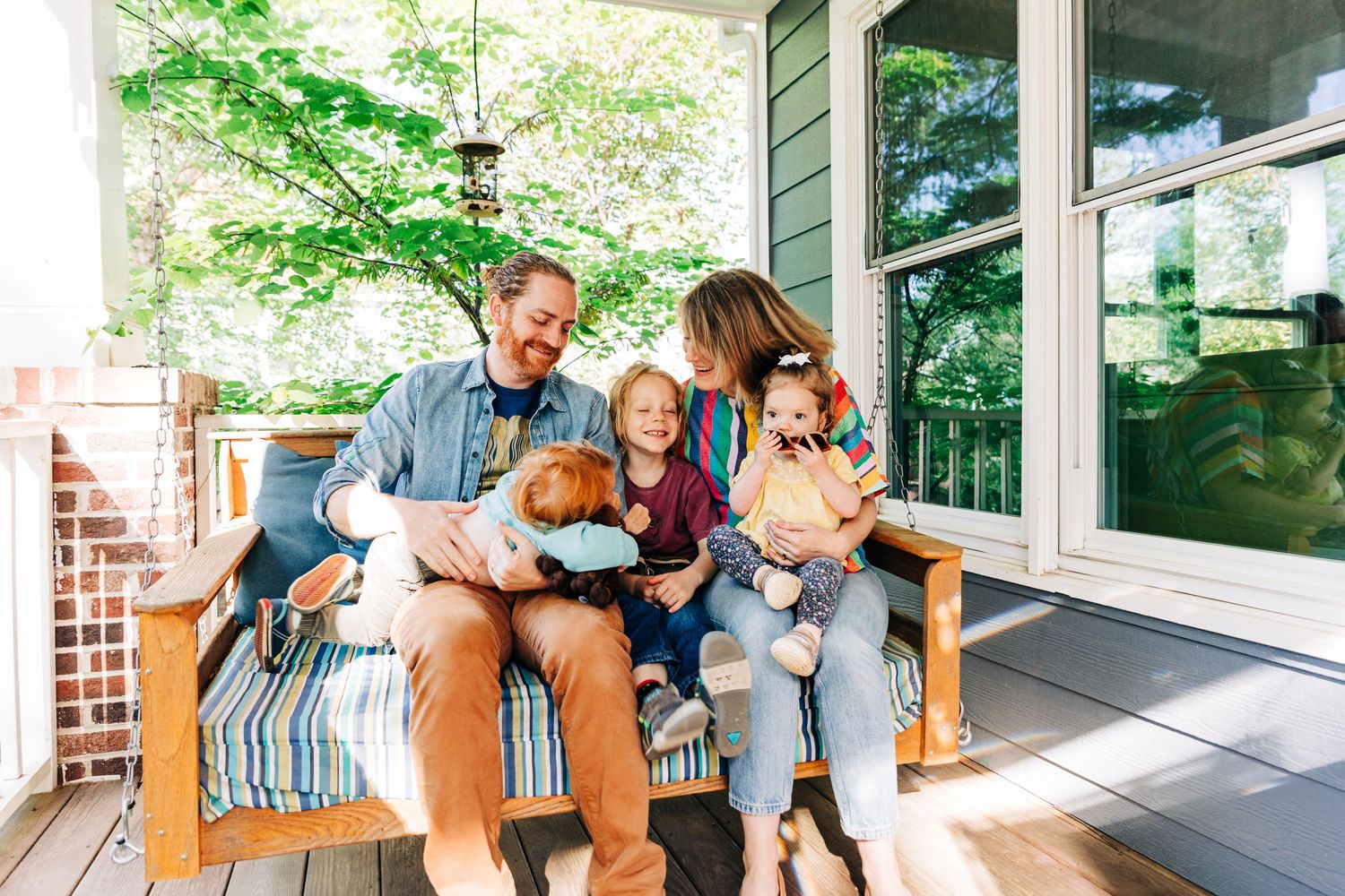 Happy family of five sitting on a sunny porch, smiling and enjoying time together outdoors in Charlotte, NC for photo session.