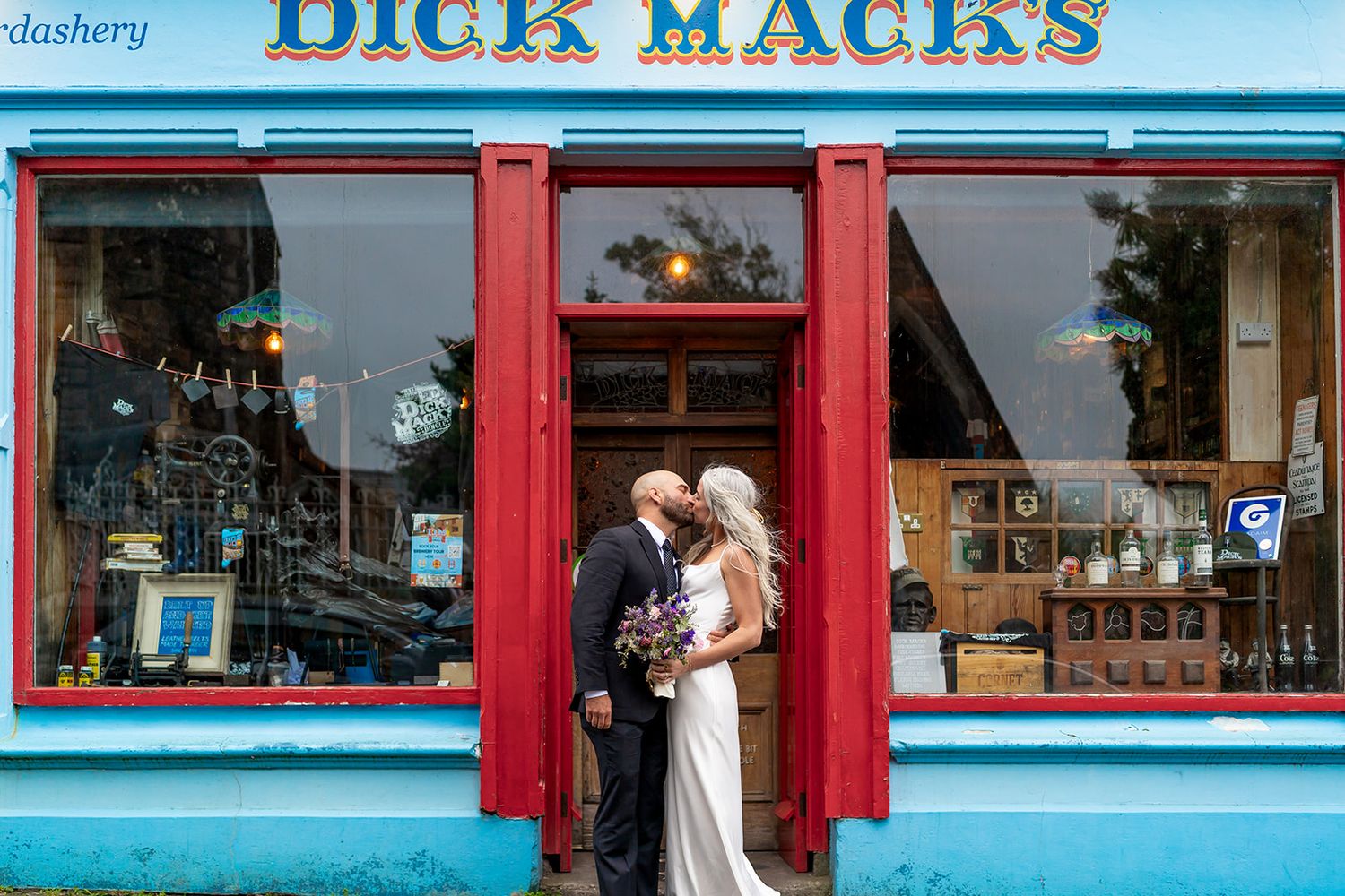 A bright blue and red storefront with large windows displays Dick Mack's signage on a traditional Irish pub building.