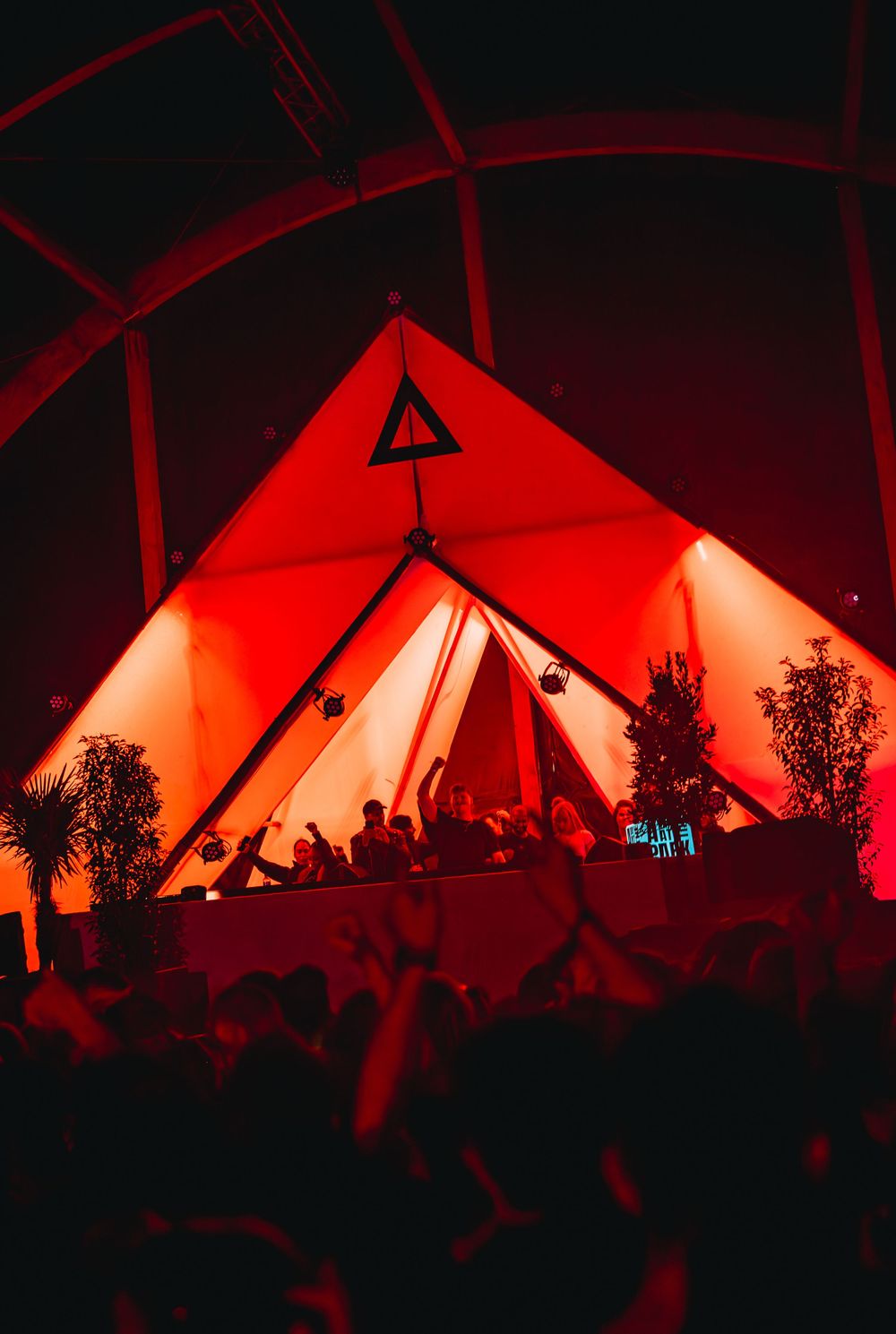 Red-lit pyramid-shaped DJ stage at Mysteryland festival with crowd silhouettes in the foreground.