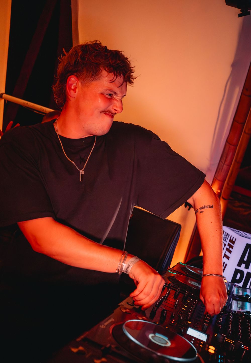 Young male DJ focused on mixing tracks at a DJ console under warm golden stage lighting.