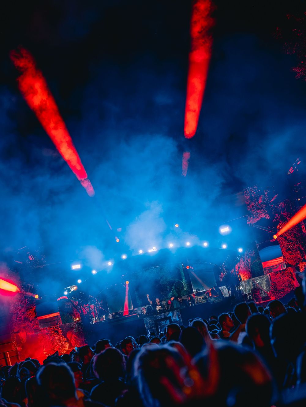 Festival crowd under dramatic blue and red stage lights with smoke effects at night concert.