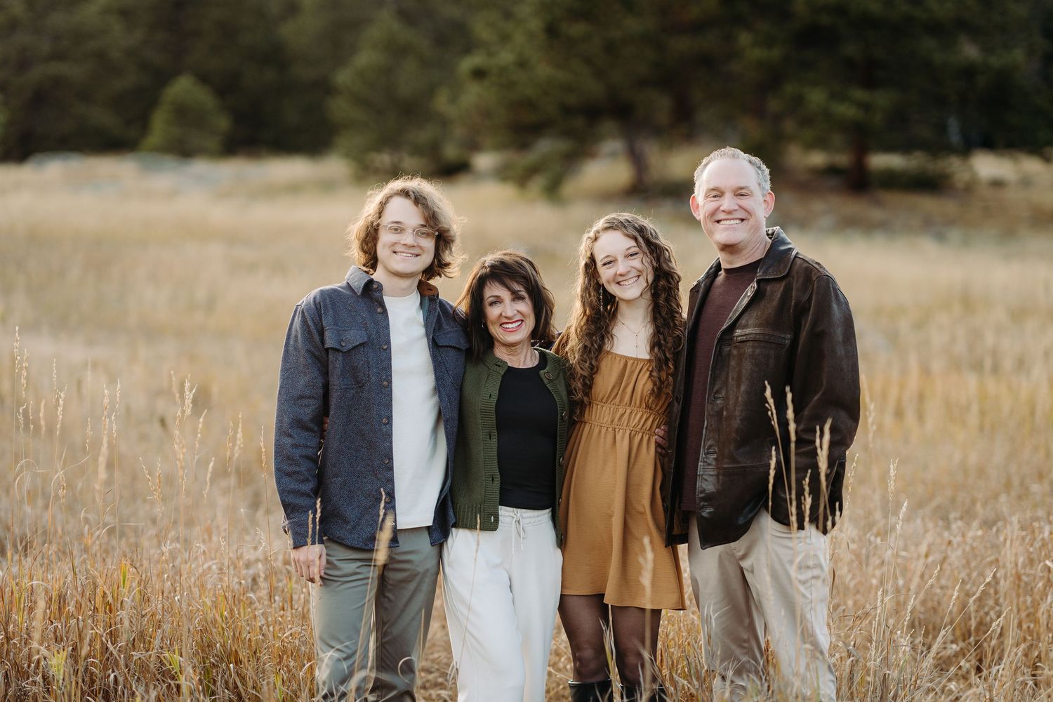 Happy family of four smiling together outdoors in a meadow, parents with two young children sitting on grass for a photography session