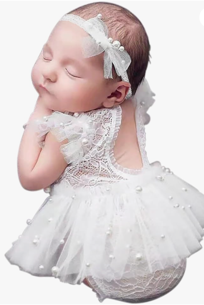 Sleeping newborn baby girl wearing white lace romper with pearl details and matching bow headband.