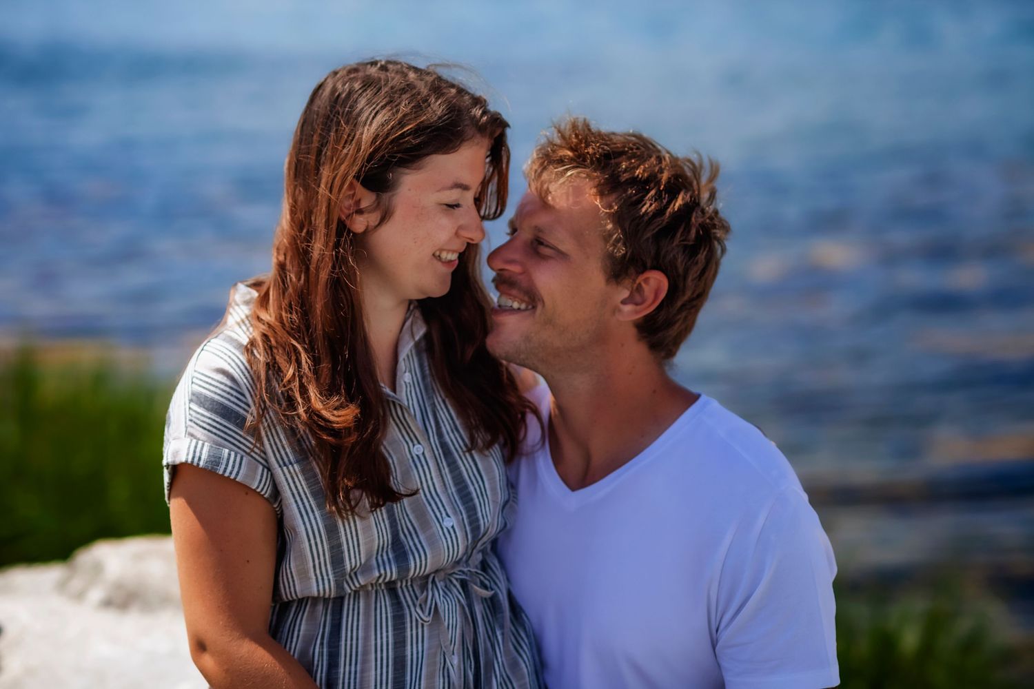 Smiling couple sharing a romantic moment by the sea on a sunny day.