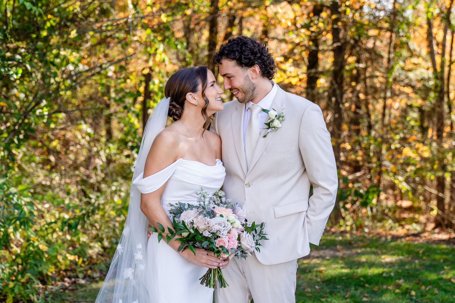Bride and groom share a romantic moment outdoors in autumn, bride holding a pink bouquet in a white off-shoulder gown at The Colonial Hotel.