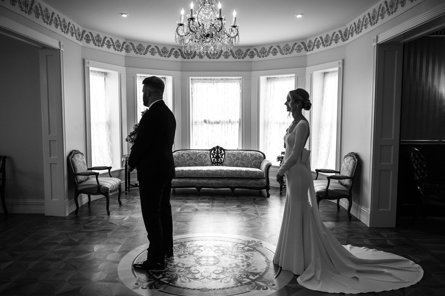 Black and white photo of bride and groom sharing a first look moment in an elegant chandelier-lit ballroom.