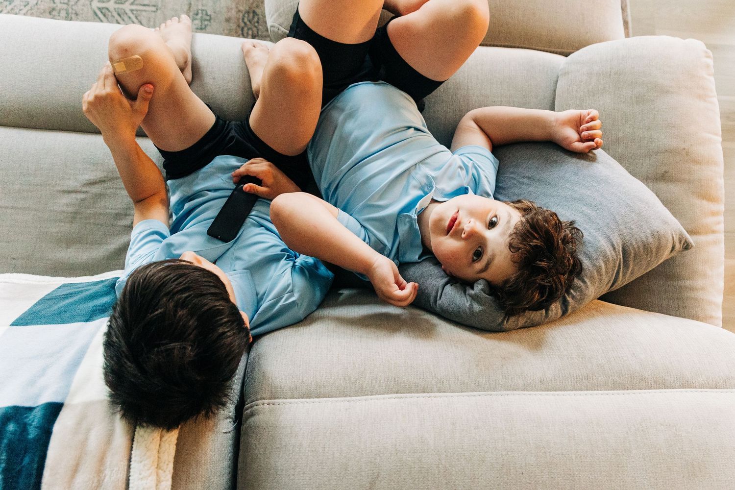 Two young children playing and laughing together on a beige couch at home.