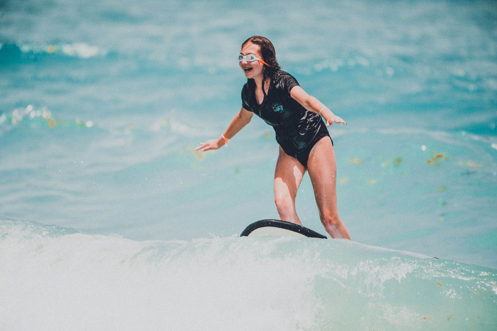Woman in black wetsuit surfing a wave in clear turquoise ocean water.