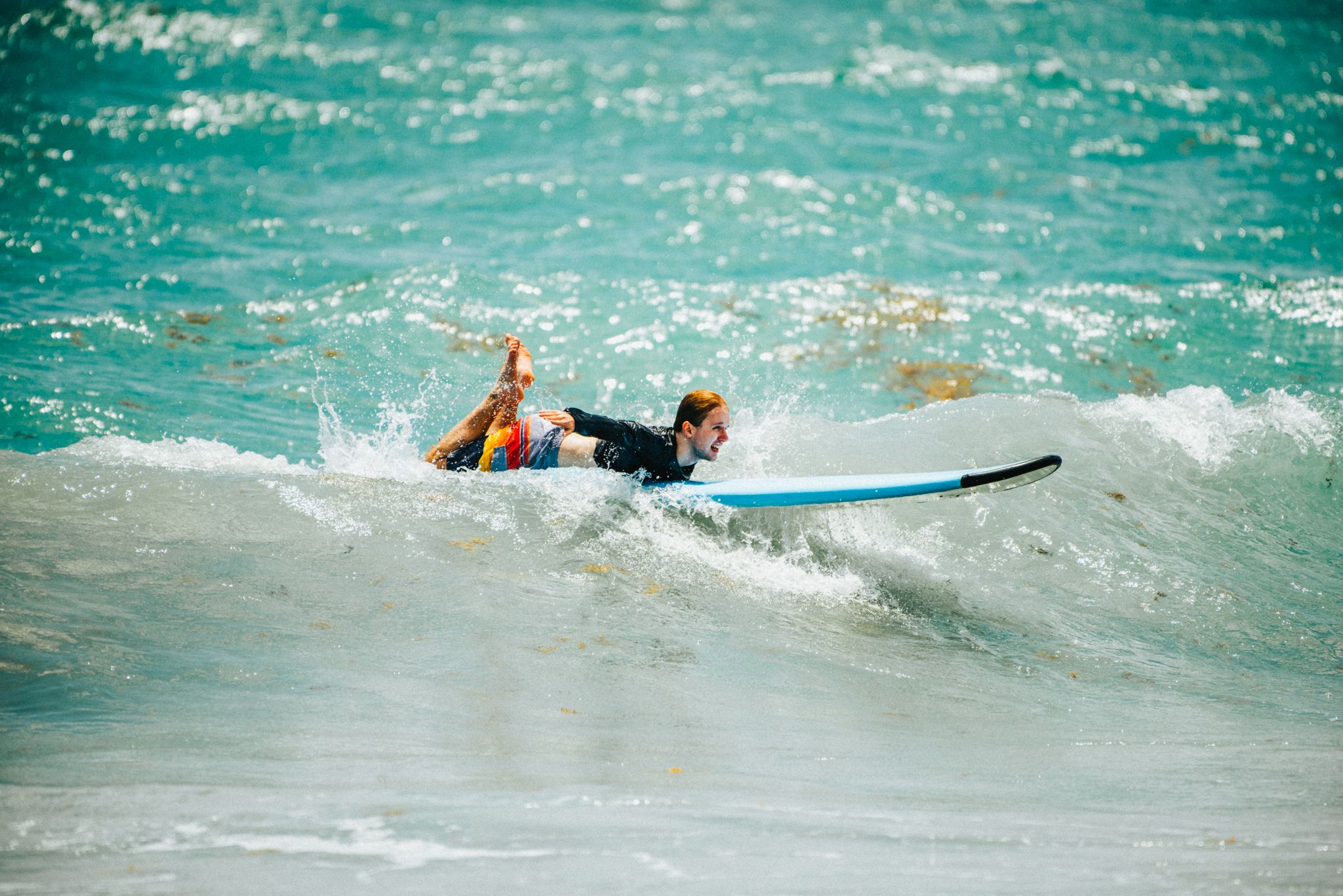 A surfer in a wetsuit and life vest paddles on a white surfboard through turquoise ocean waves.