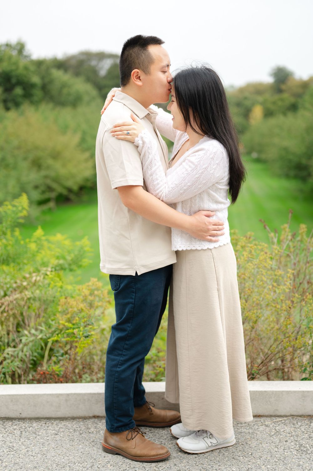 Couple sharing a kiss while embracing on a bridge overlooking a lush green landscape.